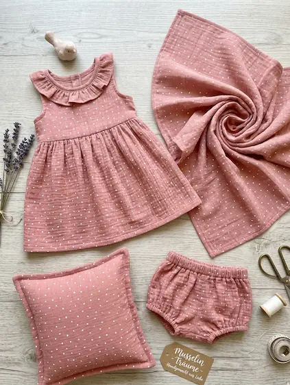 Weicher Musselin-Stoff in Altrosa mit weißen Punkten, verarbeitet als Babykleid mit Rüschen, Bloomers, Kissen und Mulltuch.