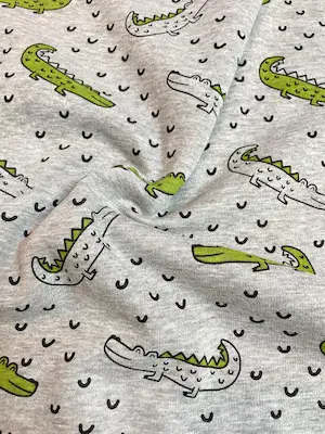 Detailaufnahme eines weichen Alpenfleece-Stoffes in Grau-Melange mit Krokodil-Motiven. Die Stofffalten zeigen die geschmeidige, schwere Qualität des Materials für Winterbekleidung.