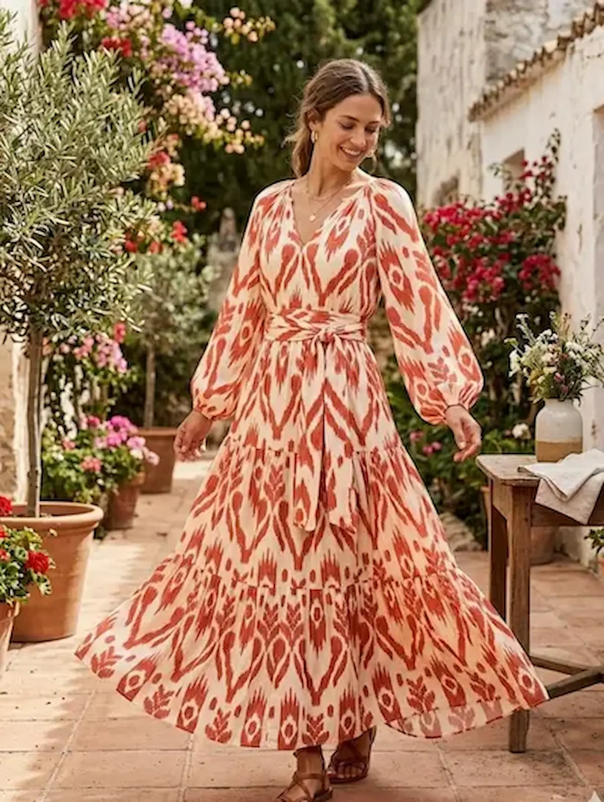 Fließendes Maxikleid aus Crinkle Viskose-Mix Meterware mit Ikat-Muster in Terrakotta und Creme, präsentiert von einer Frau in einem mediterranen Garten.