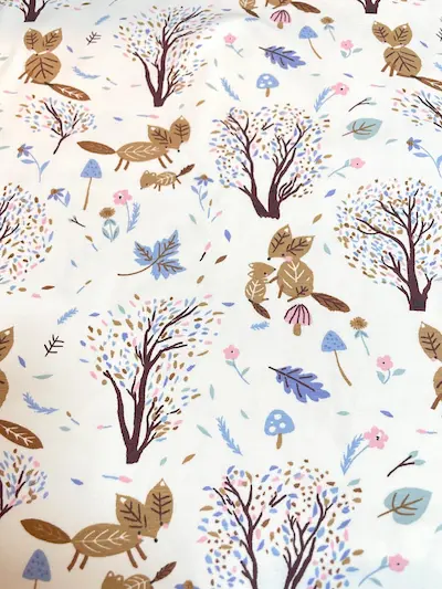 Weißer Jersey-Stoff mit Natur-Muster aus braunen Füchsen, Bäumen mit feinen Blättern, Pilzen und kleinen Blumen.