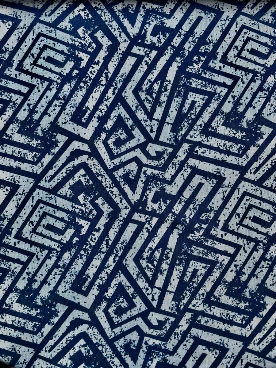 Nahaufnahme eines French Terry Stoffes mit einem abstrakten, geometrischen Labyrinth-Muster. Das Design besticht durch dunkelblaue Linien in Used-Optik auf einem hellblauen bis weißlichen Hintergrund. Hochwertiger Sommersweat als Meterware für moderne Bek