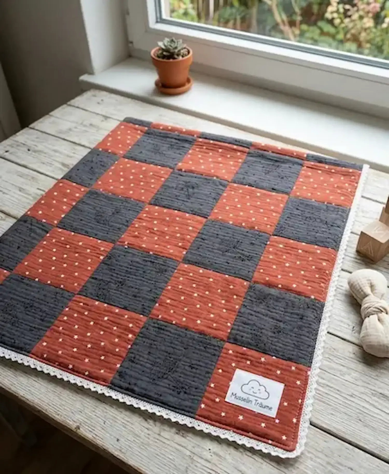 Gesteppte Patchwork-Decke aus Musselin-Stoff in Dunkelgrau mit Sonnenschirm-Motiv und Rostbraun mit Sternen auf einem rustikalen Holztisch.
