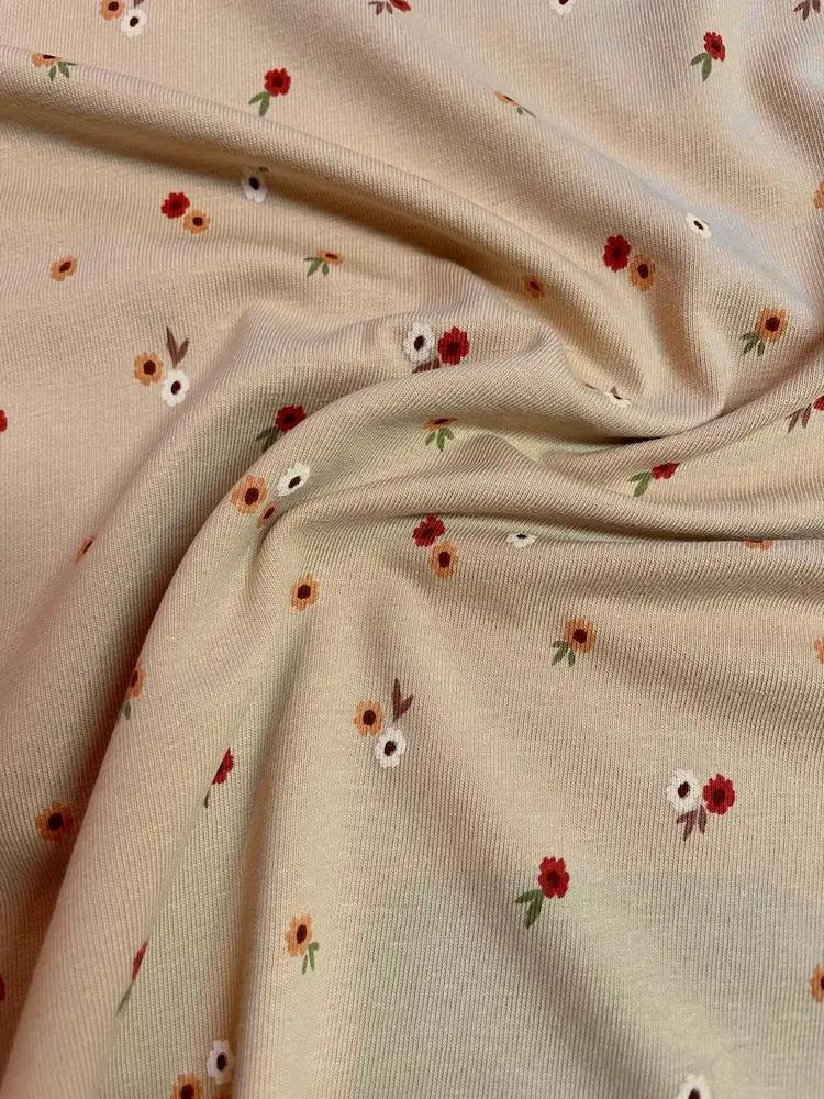 Weicher Jerseystoff in Beige mit kleinen roten und orangen Streublumen, elastische Baumwoll-Meterware für Kinderkleidung und Baby-Accessoires.