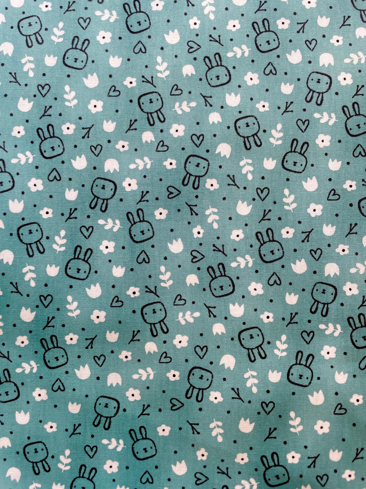 Nahaufnahme einer petrolfarbenen Baumwoll-Webware mit einem Muster aus kleinen schwarzen Hasenköpfen, weißen Herzen und zarten floralen Elementen.