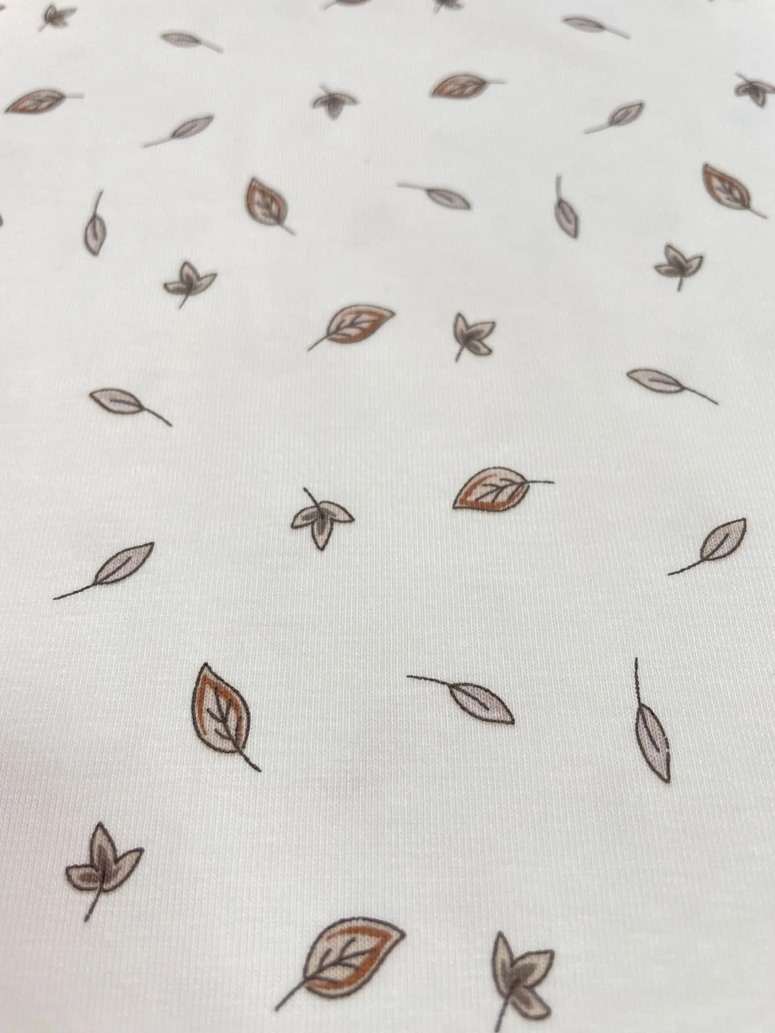 Hochwertiger weißer Jerseystoff mit kleinen, dezenten Blättern in Braun und Beige, minimalistisches Design für Babykleidung und moderne Basics.