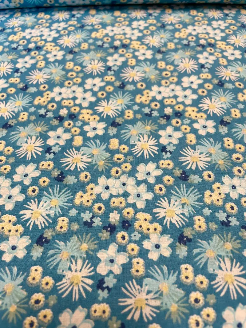 Hochwertiger Baumwollstoff als Meterware in Türkisblau mit dichtem, floralem Muster aus weißen, hellblauen und gelben Gänseblümchen und Blüten.