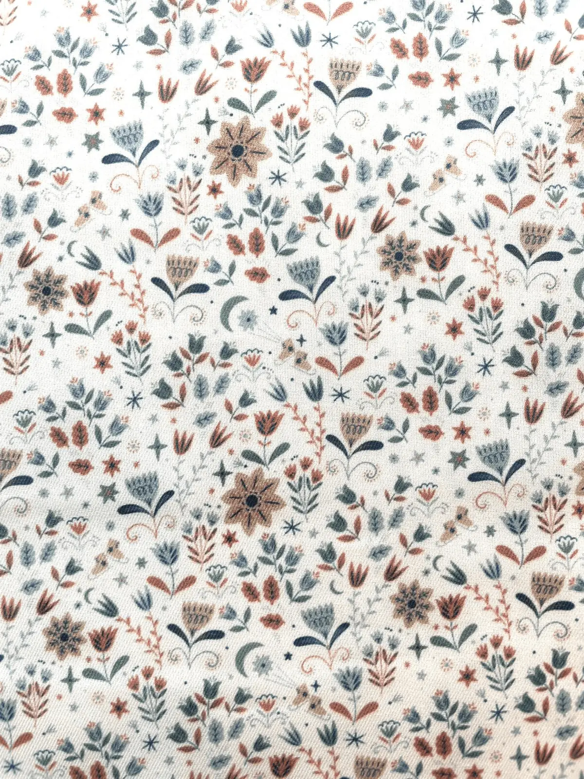 Baumwollstoff in Naturweiß mit blau-ockeren Blumen, Blättern, Sternen und Monden, 150cm breit.