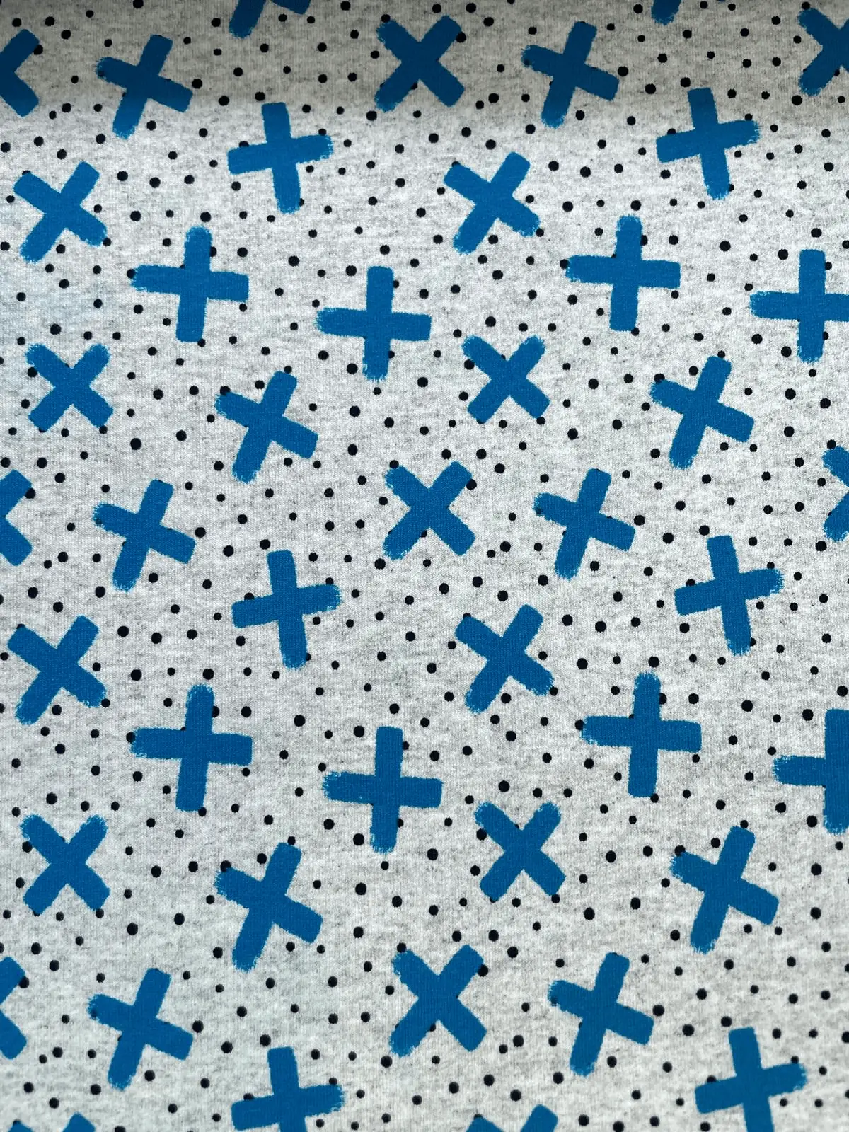 Weicher French Terry Sommersweat in Grau Meliert mit einem grafischen Muster aus blauen Kreuzen im Pinselstrich-Look und kleinen schwarzen Punkten.