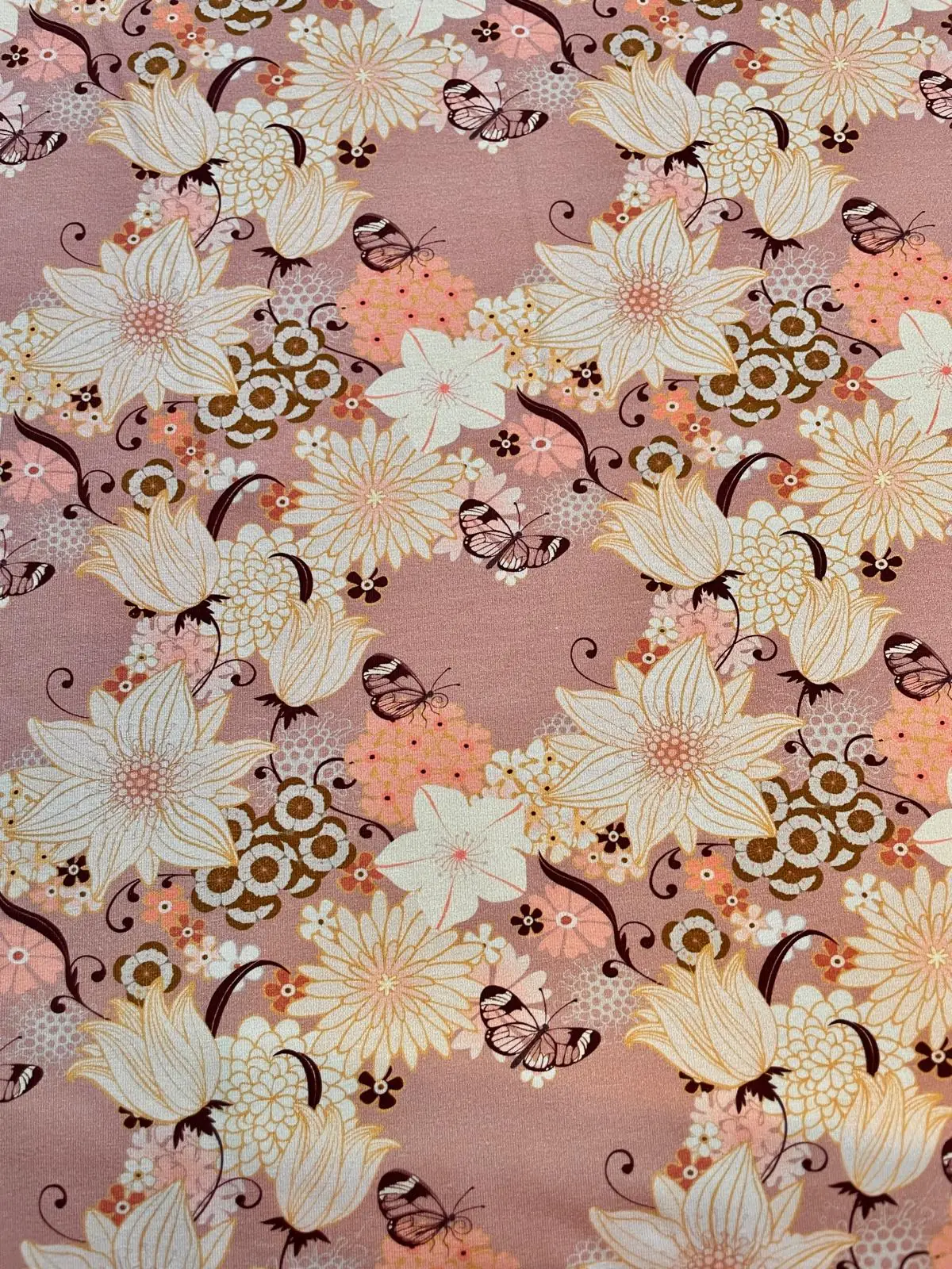 Weicher Jersey-Stoff als Meterware in Altrosa, bedruckt mit einem detailreichen, asiatisch angehauchten Vintage-Muster. Zu sehen sind große cremeweiße Blüten, filigrane Schmetterlinge, kleine orangefarbene Akzentblumen und geschwungene braune Ranken.