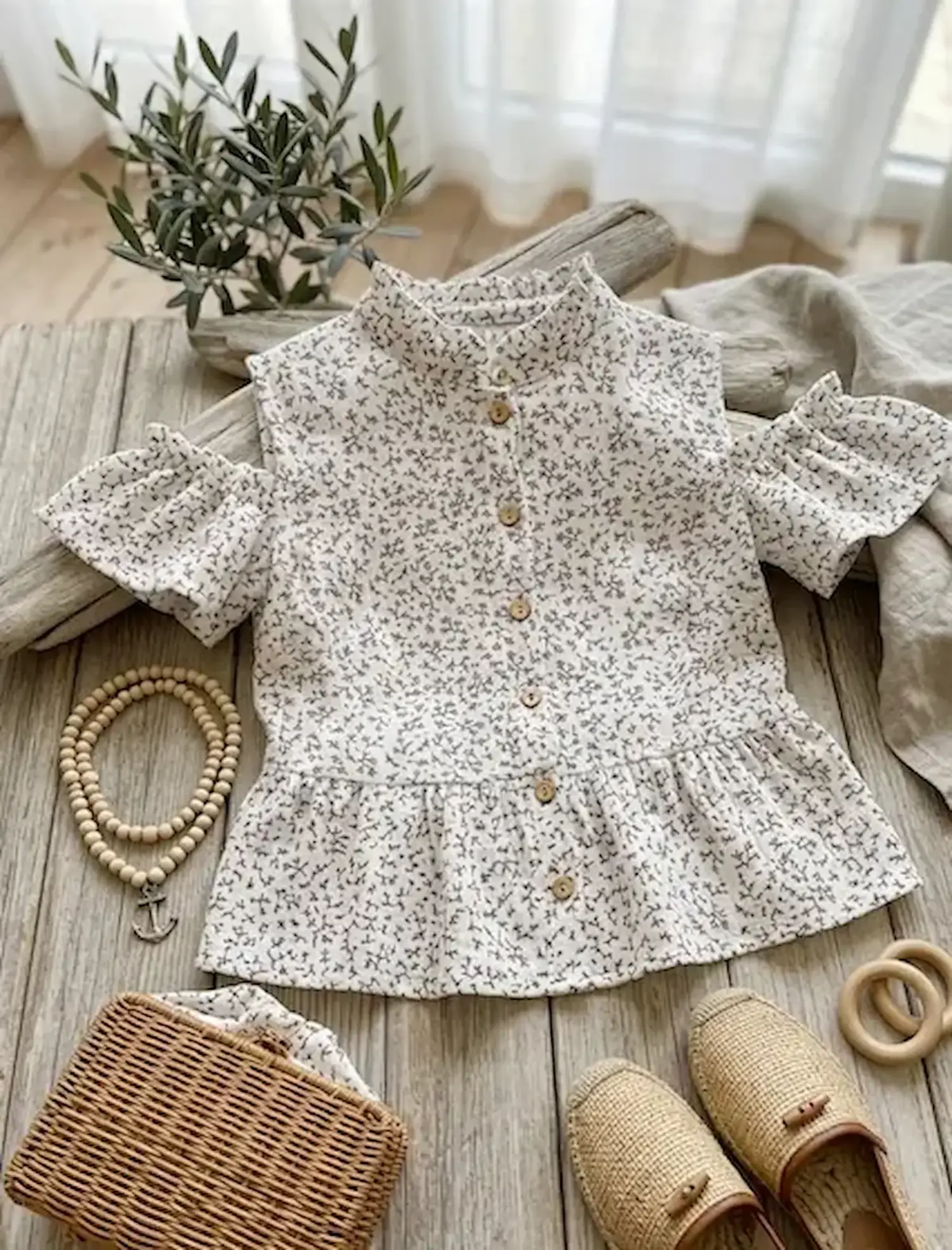 Kinderbluse aus grau-weißem Musselin mit schwarzem Zweige-Print und Holzknöpfen, flach liegend auf hellem Holz als Beispiel für Musselin-Meterware im Natur-Look.