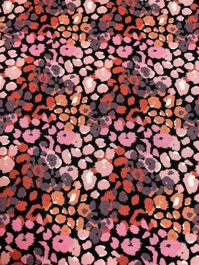 Draufsicht auf das bunte Leoparden-Muster des Jersey-Stoffs mit Flecken in Pink, Apricot, Flieder und Weiß auf schwarzem Grund.