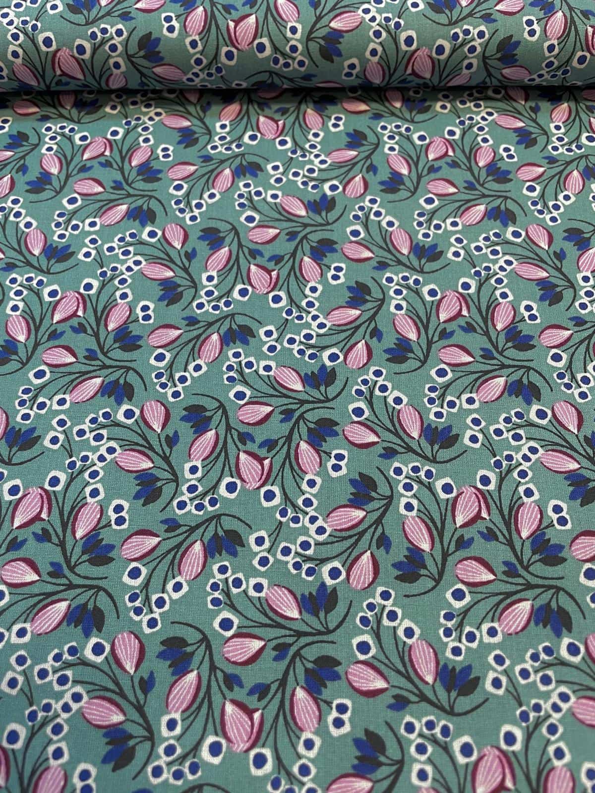 Leicht schräg von oben fotografierte Baumwoll-Webware als Meterware auf einer Stoffrolle, mit einem gleichmäßigen, floralen Allover-Muster aus altrosafarbenen Blütenknospen, dunkelblauen Blättern und weißen Beeren auf petrolfarbenem Grund.