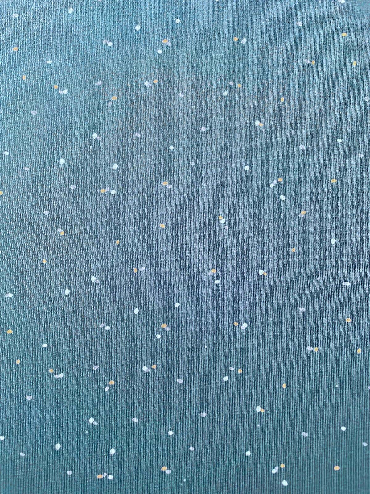 Nahaufnahme eines blaugrauen Jerseystoffs mit kleinen weißen und goldgelben Sprenkeln, Meterware für Bekleidung.