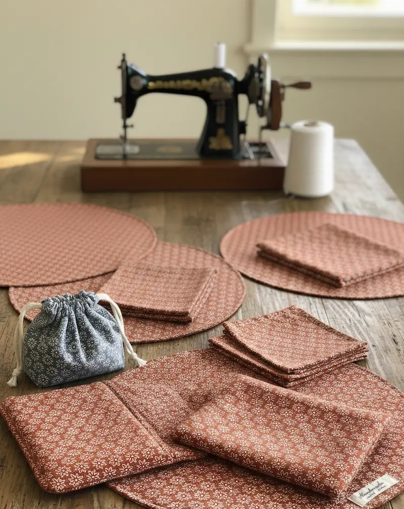 Selbstgenähte runde Tischsets und Servietten aus rostbraunem Baumwollstoff mit weißem Retro-Blumenmuster auf einem Holztisch mit alter Nähmaschine.