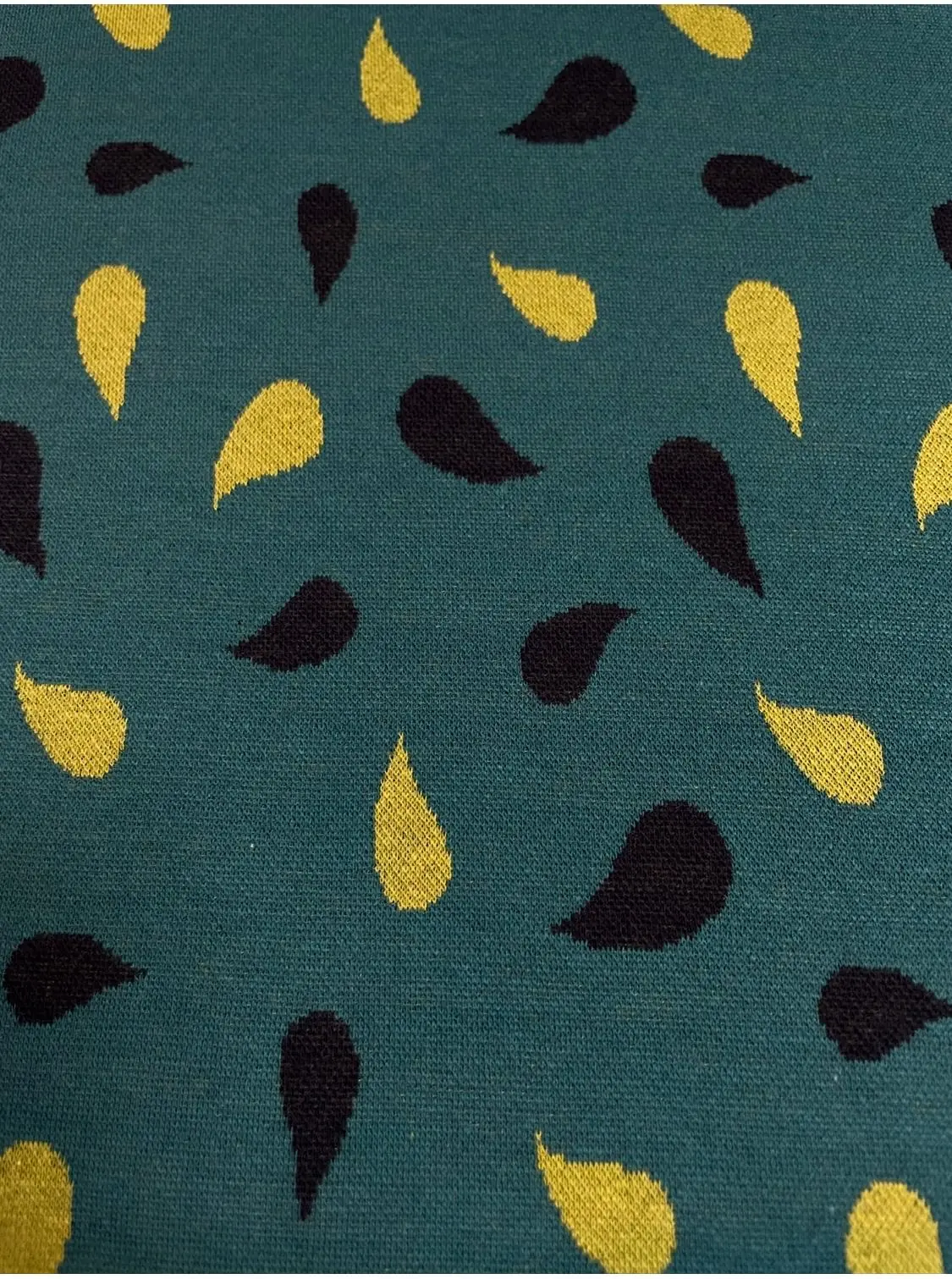 Hochwertiger Jacquard-Strickstoff in dunklem Petrol mit einem abstrakten Tropfenmuster (oder Paisley-Elementen) in Senfgelb und Schwarz. Die detailreiche Strickstruktur des blickdichten Stoffes ist gut erkennbar. Ein weicher, elastischer Kleiderstoff für