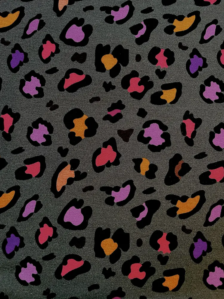 Dunkelgrauer French Terry Stoff mit buntem Leopardenmuster in Pink, Lila und Orange; glatt liegend mit Fokus auf die feine Webstruktur.