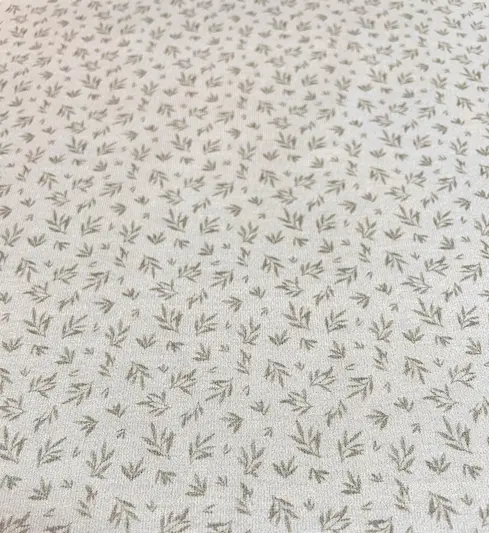 Hellbeiger Jersey-Stoff mit einem feinen, minimalistischen Muster aus kleinen graubraunen Blättern. Die gleichmäßige Anordnung der grafischen Zweige auf dem hellen Untergrund wirkt ruhig und modern, ideal für zeitlose Basic-Kleidung.