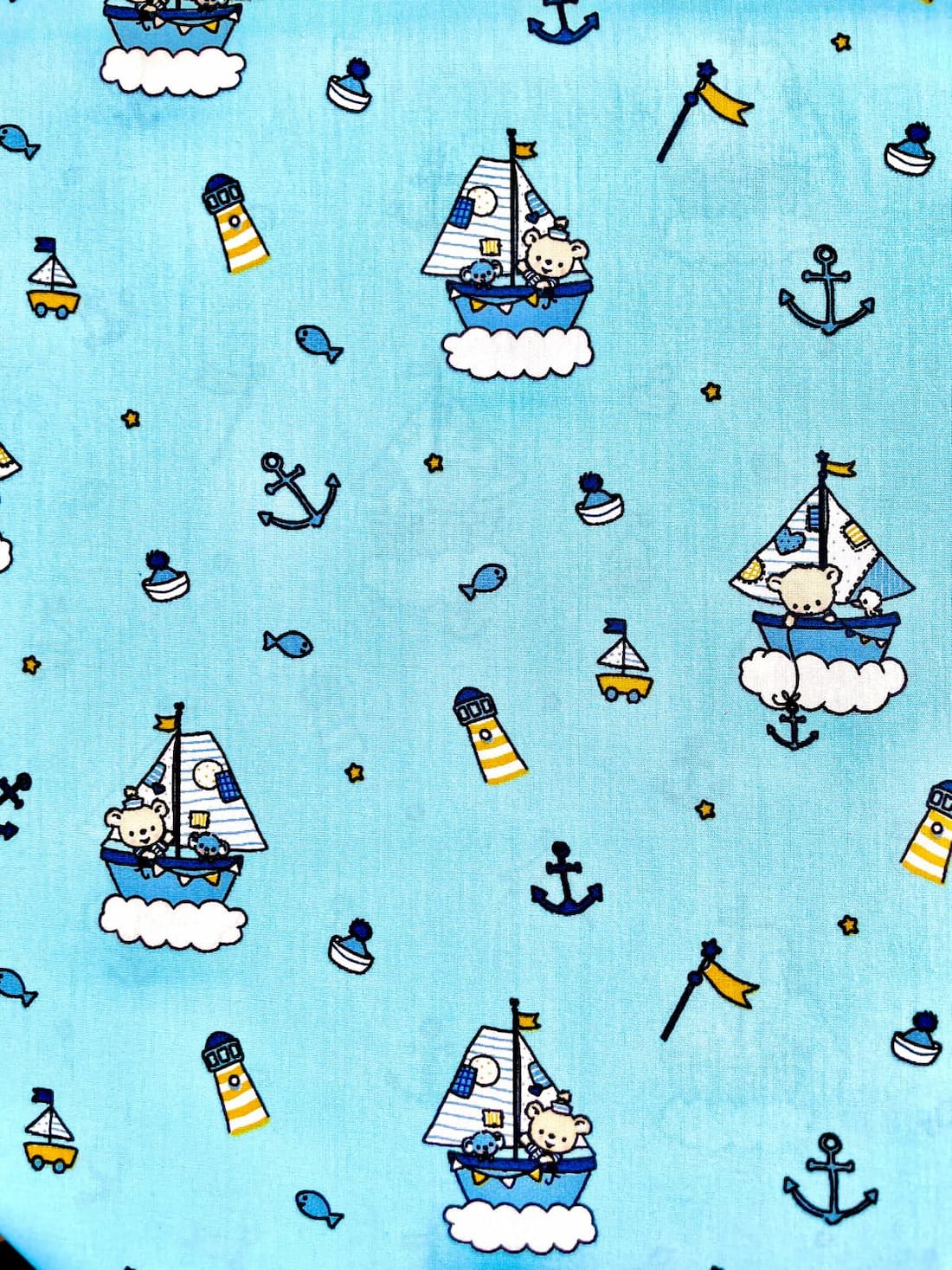Nahaufnahme eines hellblauen Baumwoll-Popeline mit maritimem Muster: Illustrationen von Teddybären in Segelbooten, gestreiften Leuchttürmen und kleinen Ankern.