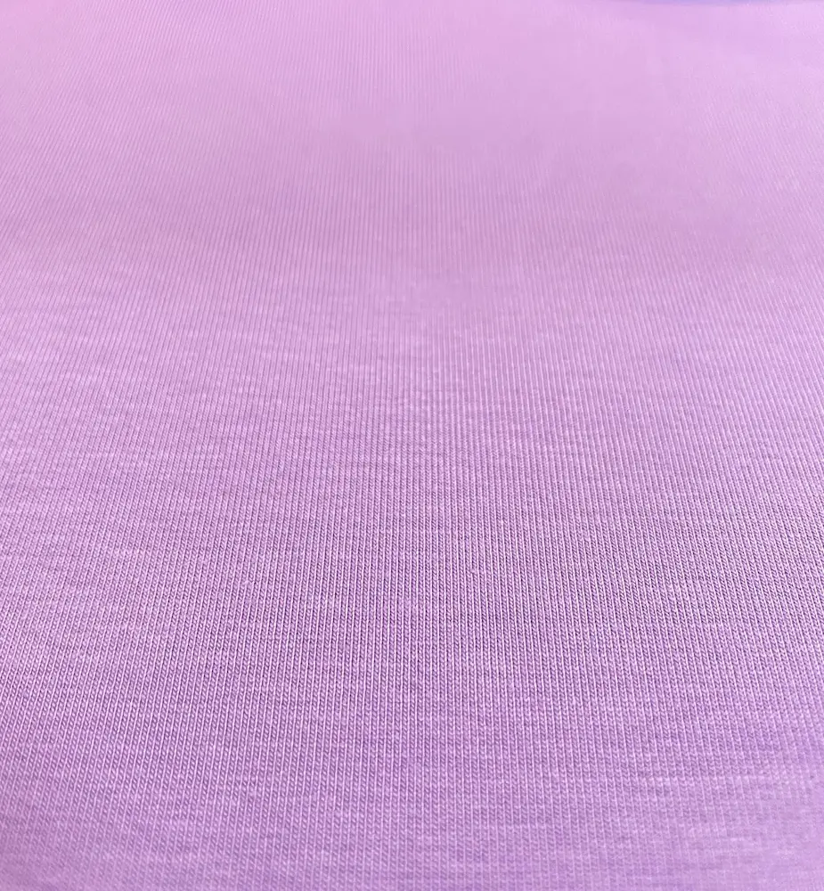 Eine detailreiche Nahaufnahme von einem unifarbenen, fliederfarbenen Baumwolljersey-Stoff als Meterware mit einer gleichmäßigen, glatten Oberfläche.
