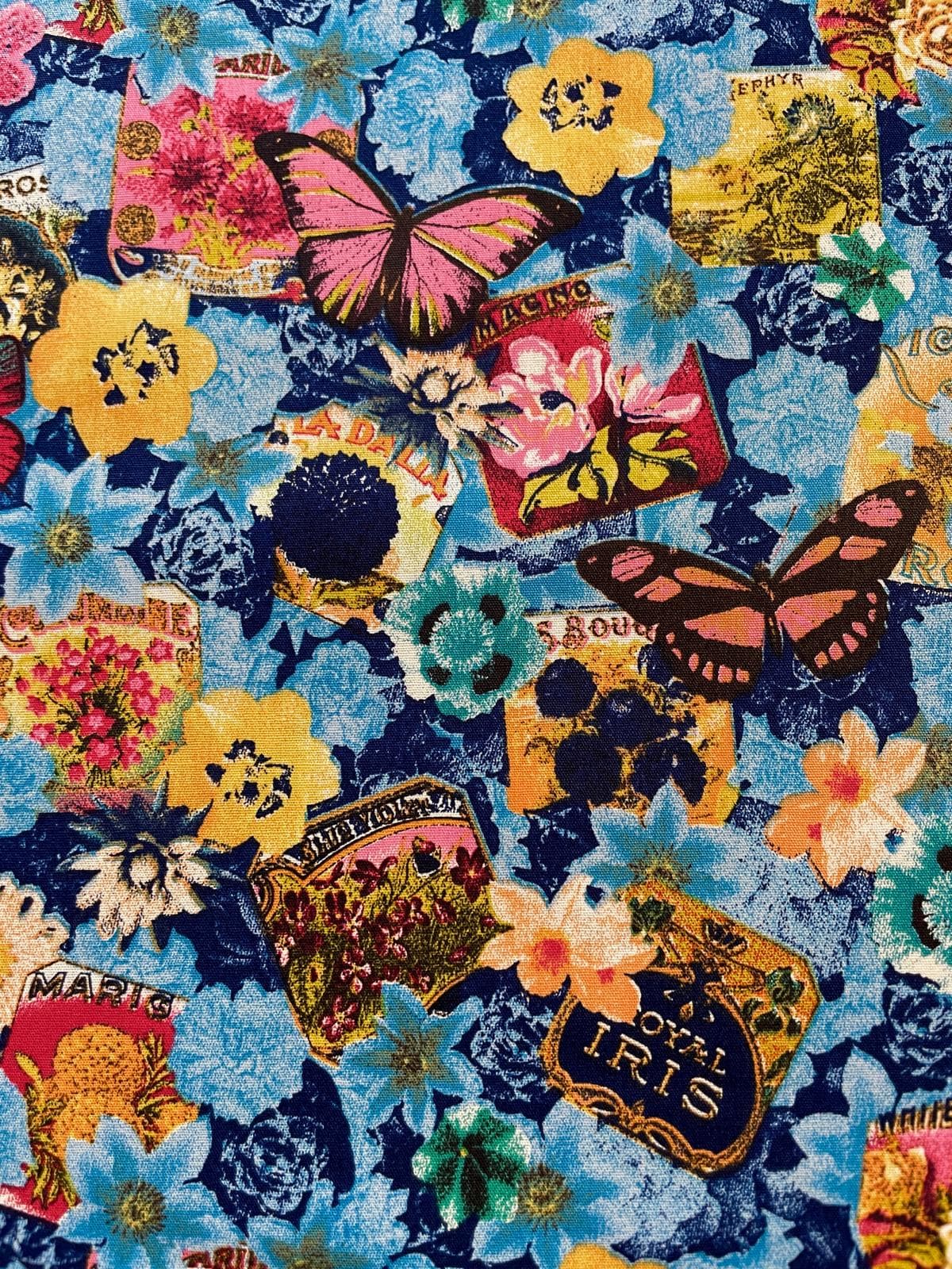 Hochwertige Baumwollstoff-Meterware in Blau mit einem lebendigen Vintage-Botanical-Druck aus bunten Blumen, Schmetterlingen und floralen Samenschildern im Retro-Stil.