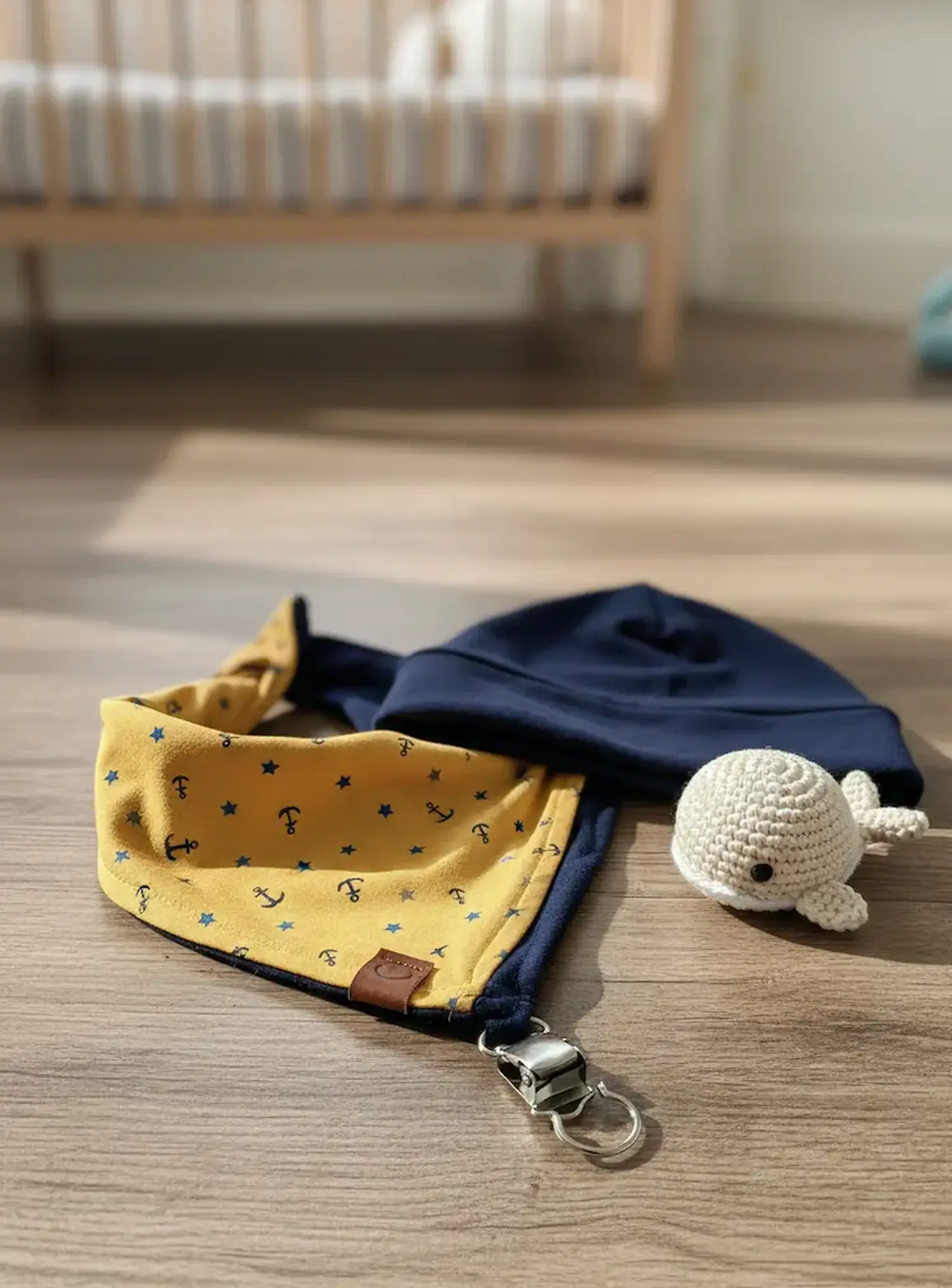 Ein selbstgenähtes Baby-Wendehalstuch aus senfgelbem Jerseystoff mit Ankern und Sternen sowie eine passende dunkelblaue Beanie-Mütze liegen auf einem Holzboden.
