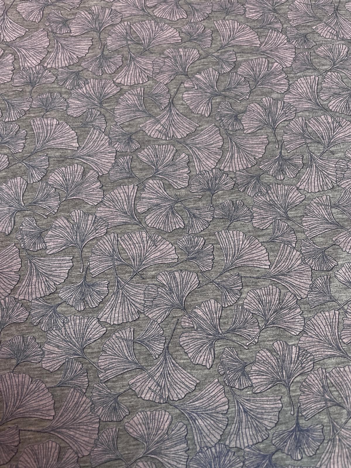Leichter, weicher Jersey-Stoff in Grau-Melange, bedruckt mit filigranen Ginkgo-Blättern in zartem Rosa und Mauve. Das elegante Natur-Motiv und die softe Haptik machen den Stoff perfekt für fließende Shirts und Tücher.