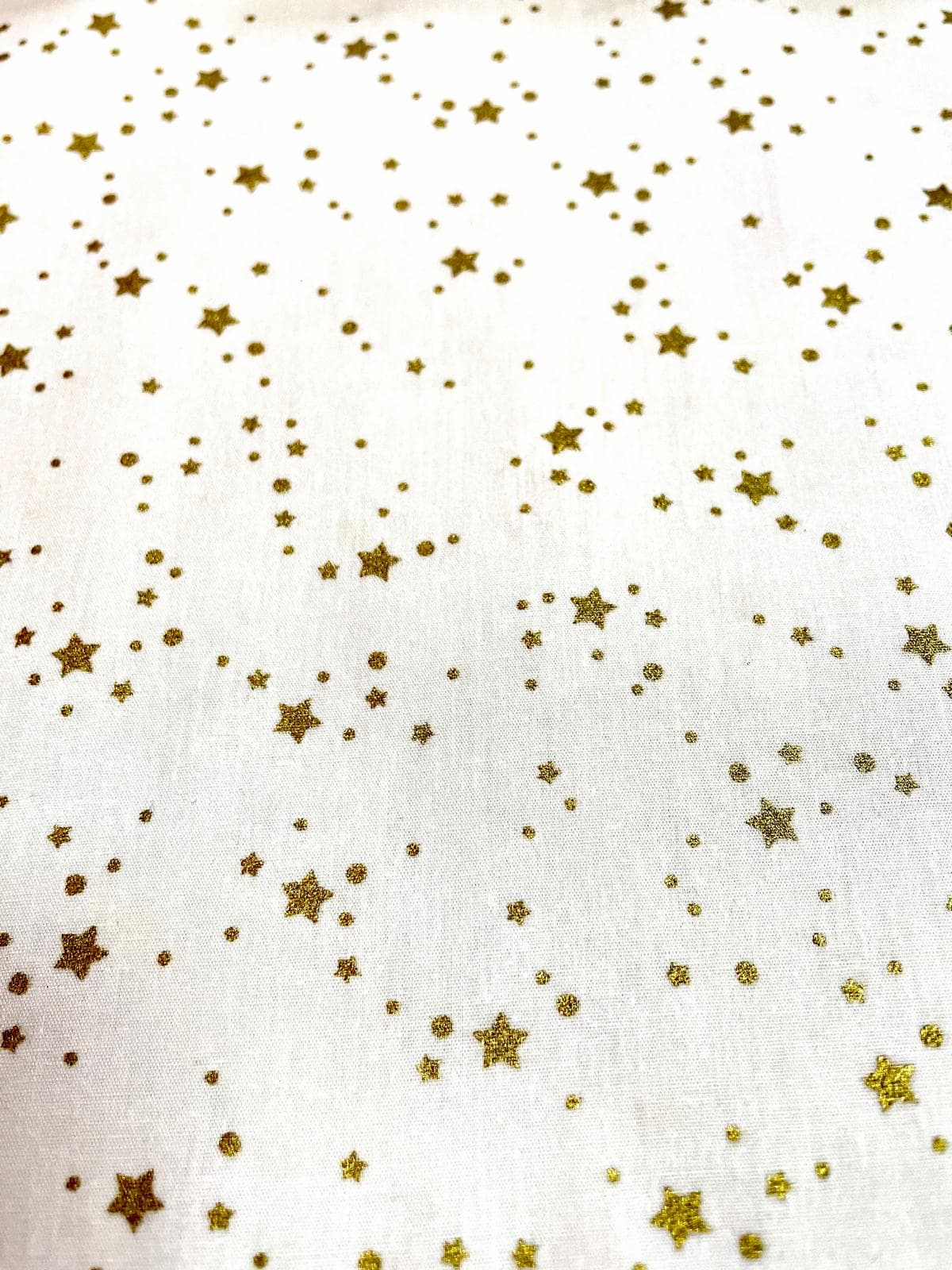 Festlicher Baumwollstoff als Meterware mit glitzernden goldenen Sternen und kleinen Punkten in verschieden Größen auf weißem Hintergrund.