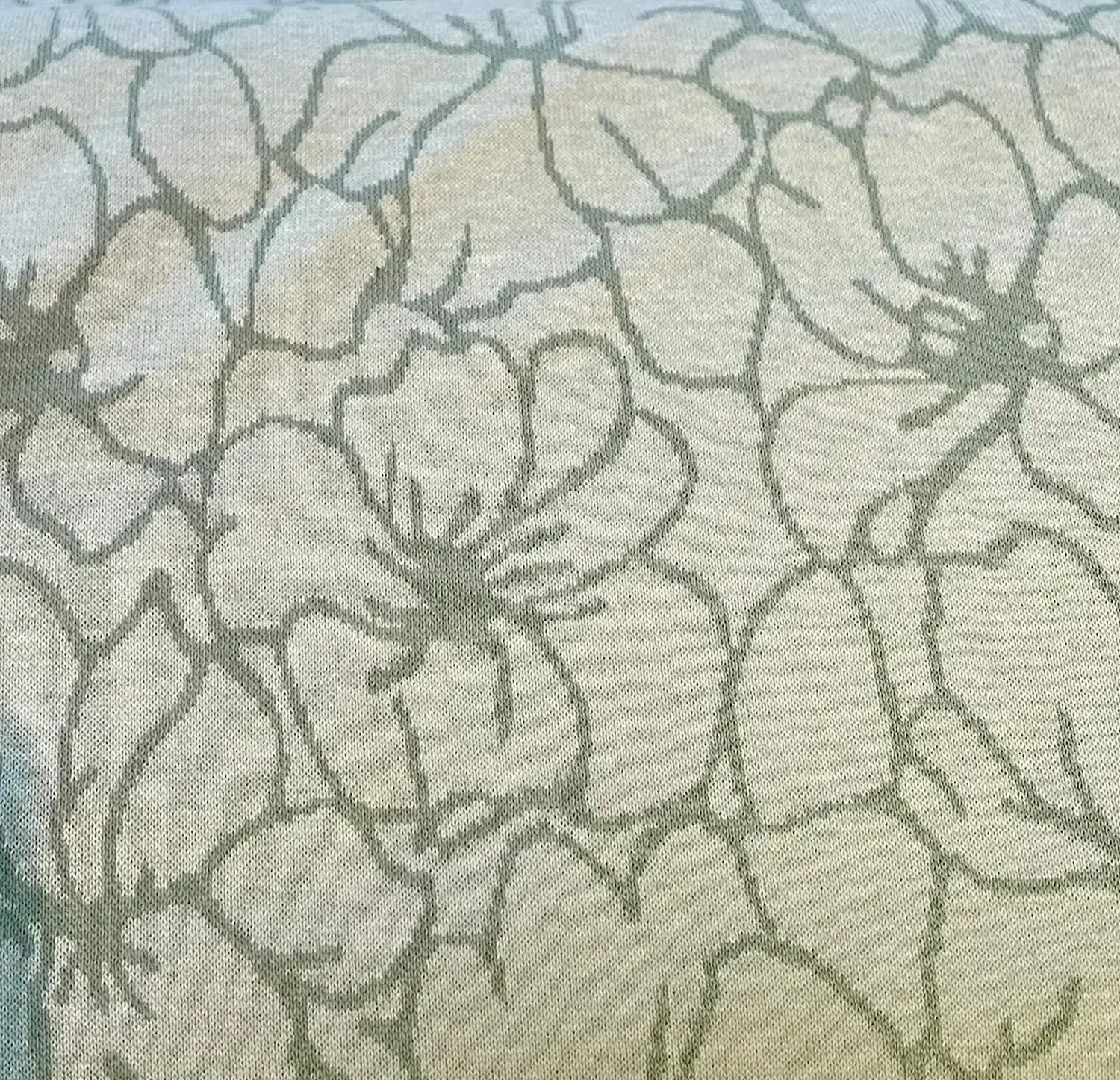 Hochwertiger Strickjacquard-Stoff mit großflächigem Blumenmuster. Die Konturen der Blüten sind in Dunkelgrün auf einem melierten Hintergrund in Hellgrün und Beige gestrickt.