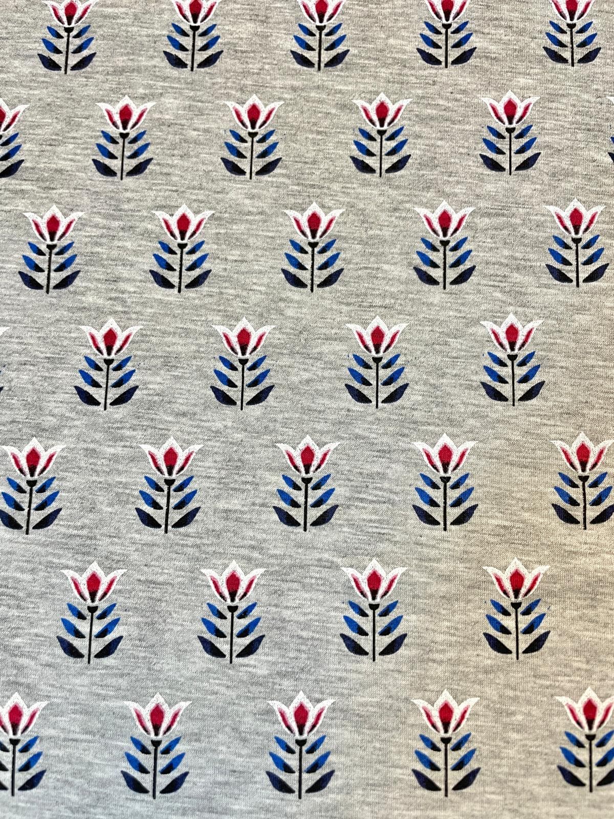 Hochwertiger Baumwolljersey als Meterware in Grau-Meliert, bedruckt mit einem regelmäßigen, geometrischen Retro-Muster aus rot-weißen Tulpen und dunkelblauen Blättern. Ideal für Bekleidung wie Shirts, Kleider und Kinderkleidung.