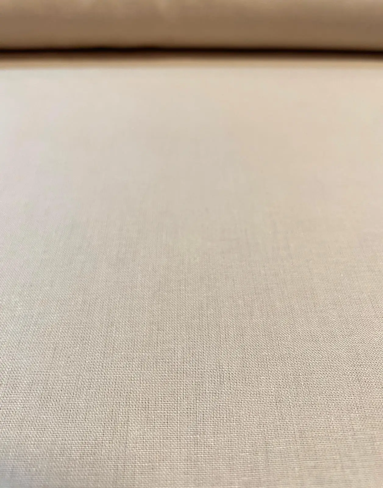 Nahaufnahme von feiner Baumwoll-Popeline als Meterware in einem hellen Beige oder Sandton. Die gleichmäßige, glatte Webstruktur des unifarbenen Baumwollstoffs ist im Vordergrund detailreich sichtbar. Ideal für Blusen, Hemden und Dekoration.