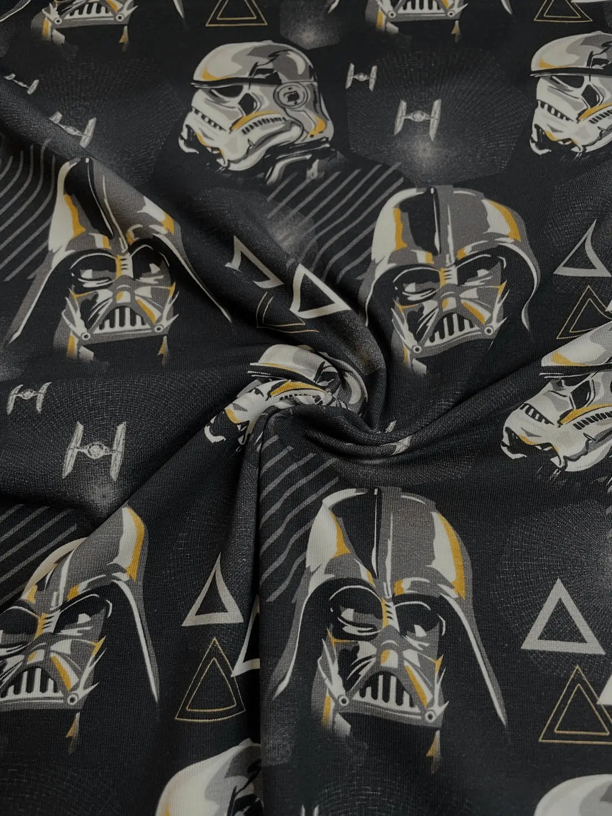 Ein kunstvoll drapierter, schwarzer Baumwolljersey-Stoff mit Faltenwurf, bedruckt mit Darth Vader Masken, Stormtrooper Helmen und TIE-Fightern.