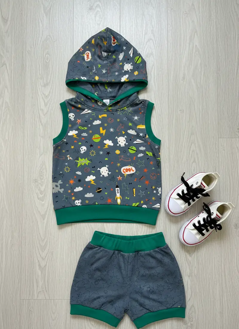 Handgenähtes Sommer-Set für Kinder aus elastischem Baumwolljersey in Blaugrau. Das Set besteht aus einer ärmellosen Hoodie-Kapuzenweste mit buntem Comic-Streumuster (Raketen, Totenköpfe, „COOL“) und einer passenden kurzen Shorts mit dezenten Sternen-Kontu