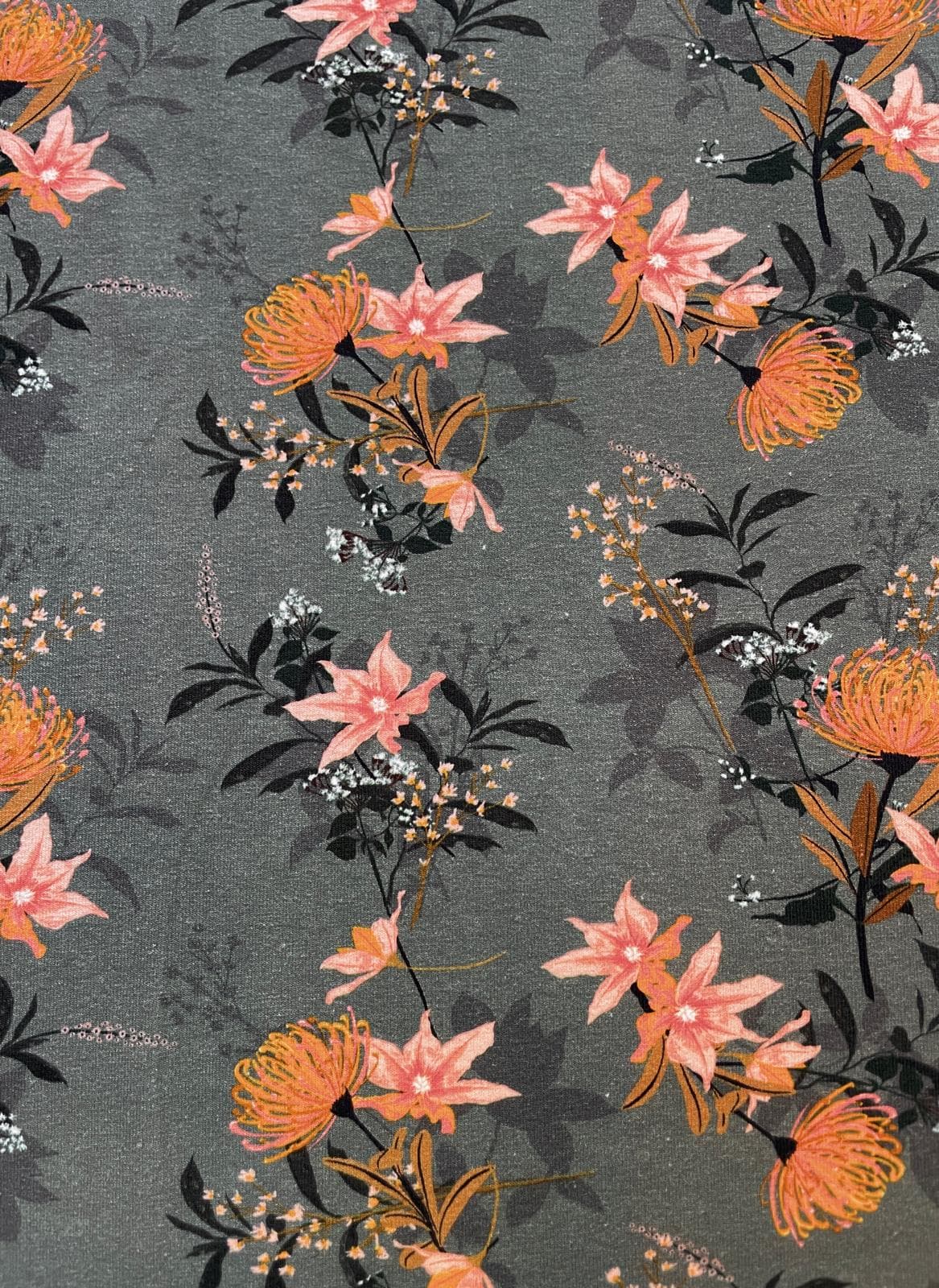 Olivgrüner Baumwolljersey als Meterware bedruckt mit einem eleganten floralen Muster aus lachs- und ockerfarbenen Blüten sowie dunklen Blättern.