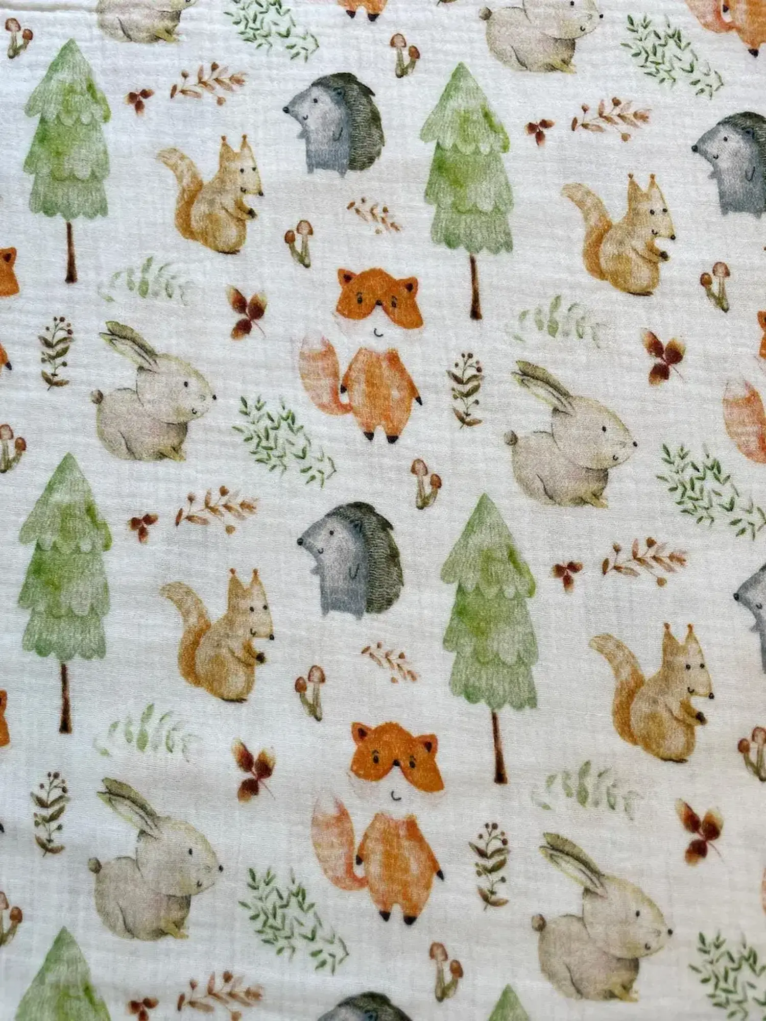 Cremefarbener Musselinstoff mit buntem Waldtiere-Print bestehend aus Fuchs, Eichhörnchen, Hase, Igel, Tannen und Pilzen. 100% Baumwolle, Double-Gauze Qualität.