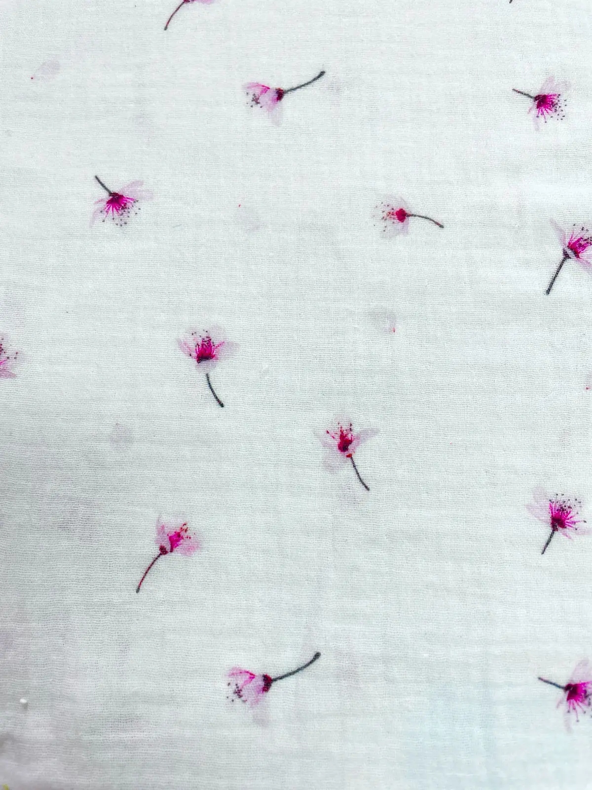 Detailaufnahme von weißem Musselin-Stoff mit zarten, fliegenden Kirschblüten in Rosa und Beere. Hochwertige Baumwoll-Meterware mit typischer Crinkle-Struktur für Babykleidung.