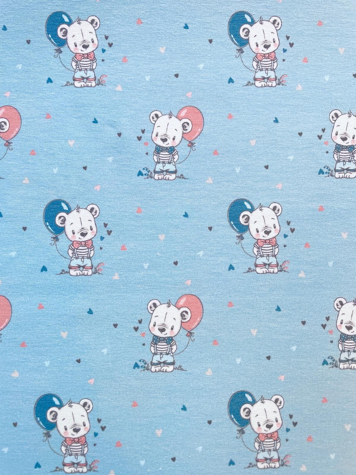 Hellblauer Baumwolljersey als Meterware bedruckt mit kleinen illustrierten Teddybären, die blaue und rosa Luftballons halten.