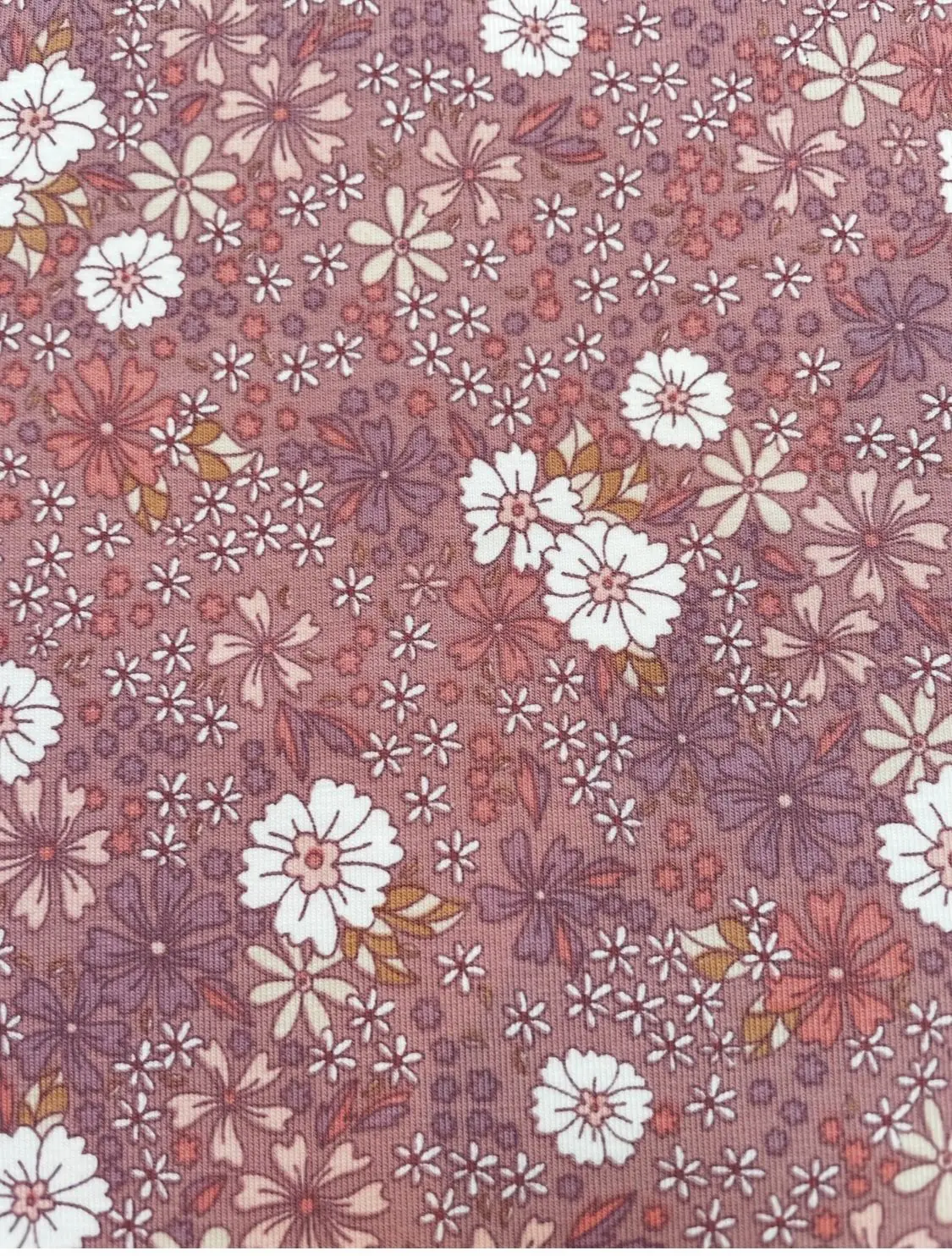 Detailreiche Ansicht eines Jersey-Stoffs mit dichtem Blumenprint in Mauve, Flieder und Weiß. Das Muster zeigt eine Vielzahl filigraner Blütenformen im romantischen Allover-Design.