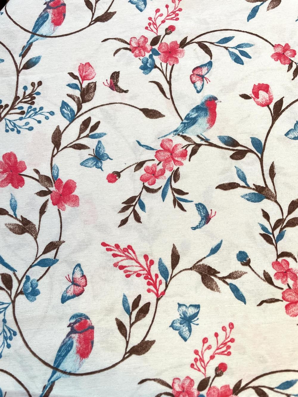 Meterware Dekostoff mit Muster aus blauen Vögeln, Schmetterlingen und rosa Blüten auf naturfarbenem Grund, Mischgewebe 195g, 138cm breit.