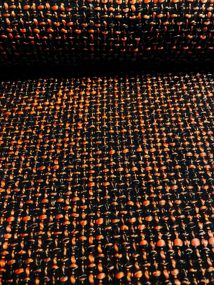 Detailansicht eines hochwertigen Bouclé-Gewebes mit kontrastreichen schwarzen und orangefarbenen Garnen in grober Struktur-Optik.