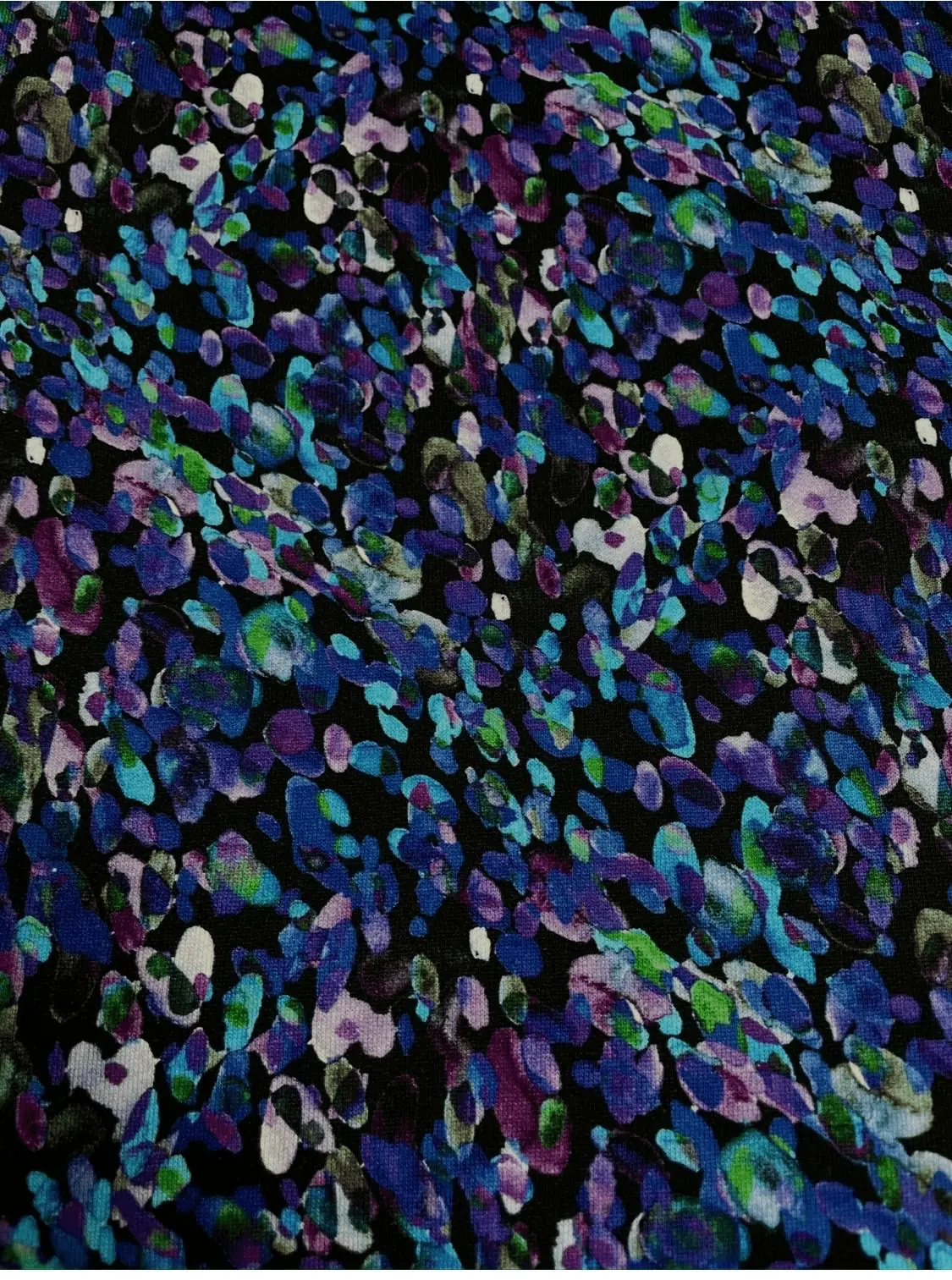 Kuscheliger Alpenfleece-Stoff als Meterware mit einem dunklen Untergrund und einem dichten, abstrakten Allover-Muster aus farbigen Tupfen, Flecken und Konfetti-Elementen in verschiedenen Nuancen von Blau, Lila, Violett und leuchtendem Grün.