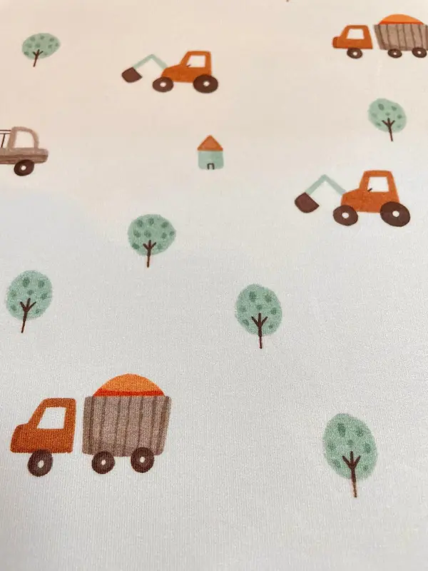 Weicher French Terry Sommersweat in sehr hellem Grau (Fast-Weiß). Das kindgerechte Muster zeigt kleine orangefarbene Bagger, Lastwagen mit Ladung, mintgrüne Bäume und kleine Häuser in einem minimalistischen Illustrationsstil. Hochwertiger, elastischer Bau