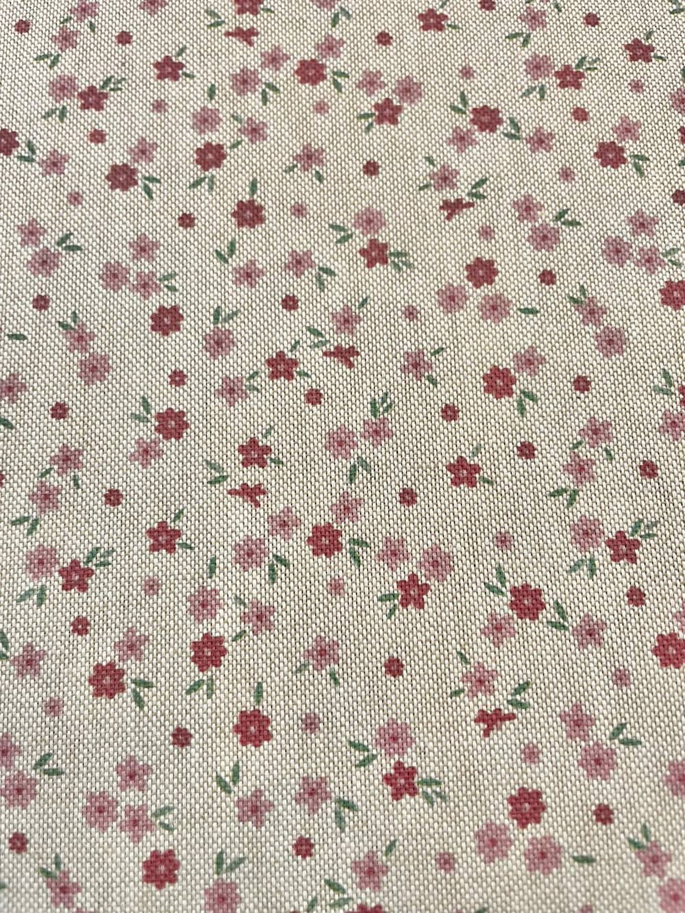 Strukturierter Dekostoff als Meterware mit kleinen, zarten Streublümchen in Rosa und Rot auf hellem Hintergrund in Leinenoptik.