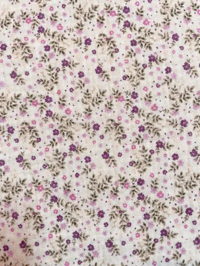 Nahaufnahme von weißem Musselin-Stoff mit kleinen lila Blumen und grünen Blättern, weiche Double-Gauze Struktur aus 100% Baumwolle.