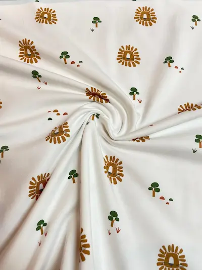 Weißer Jersey-Stoff mit freundlichen Löwenköpfen und kleinen Bäumen im Boho-Stil, weich drapiert für Kinder- und Babykleidung.