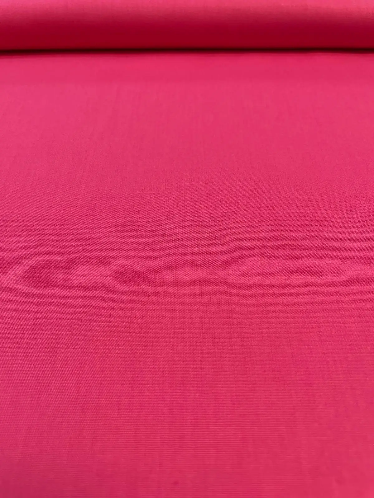 Farbenfrohe Zimmer-Dekoration aus himbeerrotem Baumwollstoff, bestehend aus einem großen runden Stoffkorb auf dem Holzboden, kleinen Sternenkissen, einem Tischläufer und Dekokissen mit weißer Pompon-Borte auf einer Fensterbank.
