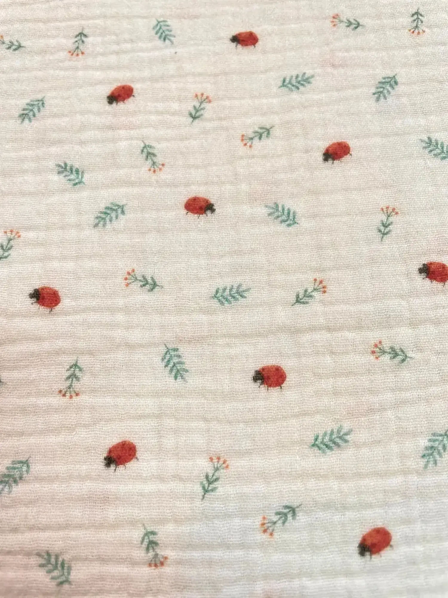 Weicher Baumwoll-Musselin in Creme mit kleinen Marienkäfern und grünen Zweigen, luftiger Double Gauze für Baby-Erstausstattung.