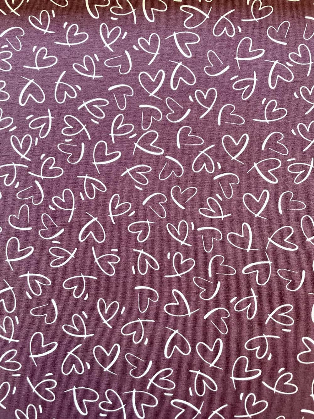 Hochwertiger violetter Jerseystoff mit weißem, handgezeichnetem Herzmuster, Meterware aus 95% Baumwolle für Damen- und Kinderbekleidung.