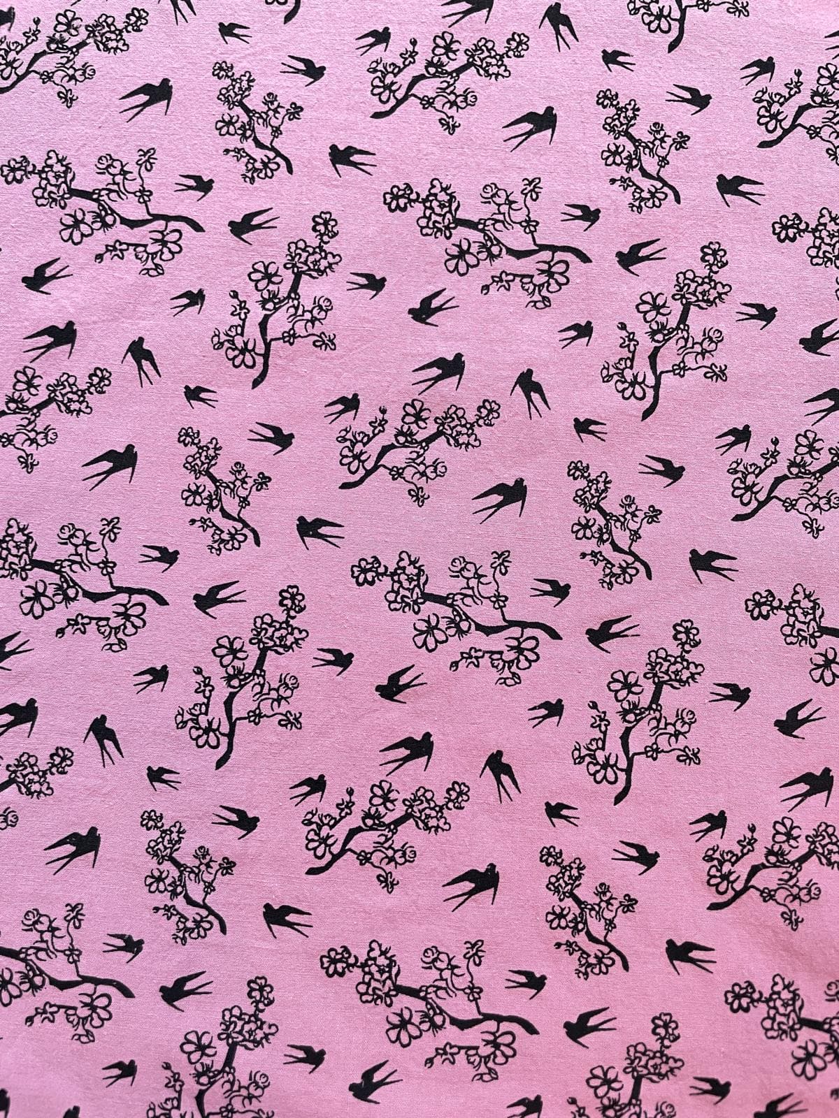 Stoffansicht einer leuchtend pinkfarbenen Kochbaumwolle, bedruckt mit schwarzen Schwalben-Silhouetten und Kirschblütenzweigen. Kontrastreiches Design aus 100% Baumwolle