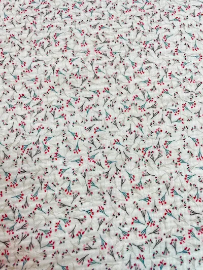 Flächenansicht von weißem Musselin-Stoff mit einem dichten, all-over Print aus filigranen Beeren-Zweigen in Rot und Blau. Zeigt die Musterwiederholung der Double-Gauze Meterware.