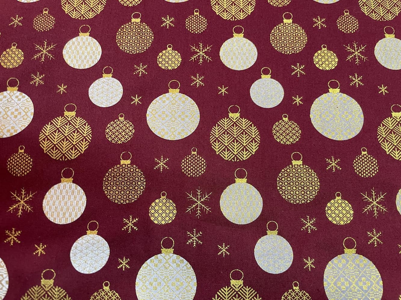 Eleganter Baumwollstoff als Meterware mit festlichen Christbaumkugeln und Eiskristallen in Gold und Weiß auf tiefem Bordeaux-Rot.